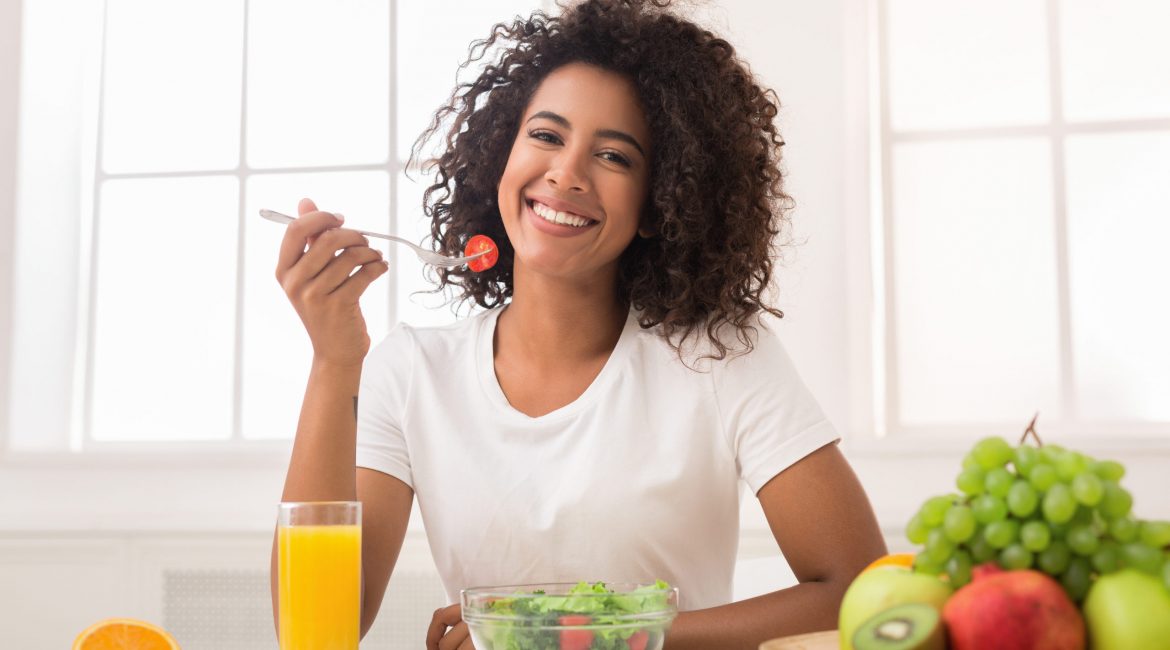 African-american woman eating vegetable salad and drinking fresh juice at home